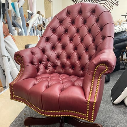 Swivel office chair reupholstered with red leather, tufted seat bach arms and decorated with nailheads